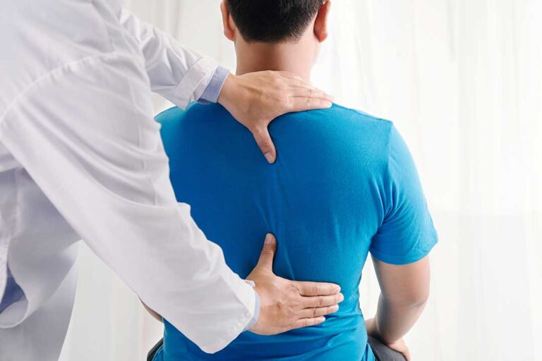 Clinician evaluates a patient’s spine movement while discussing symptoms in a bright examination room.